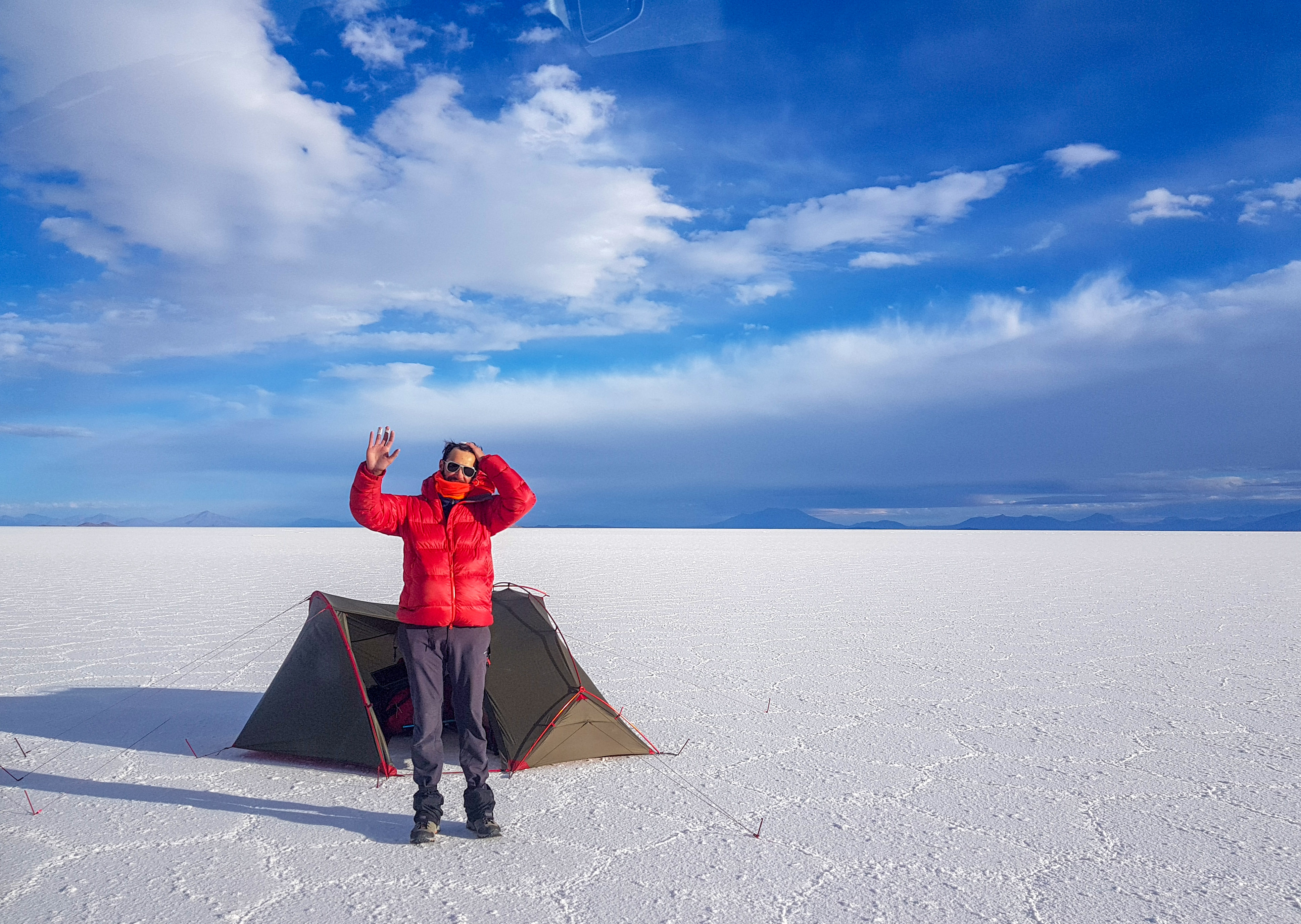 Photo d'Alban Tessier lors de son expedition dans le Salar d'Uyuni en Bolivie. Il pose souriant à côté de sa tente  au milieu du désert blanc.
