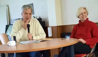 Un homme et une femme assis devant une table. l'homme tient un micro.