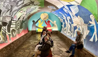 Un groupe de personnes assises dans la chapelle où est exposée l'œuvre "Guerre et Paix" de Picasso