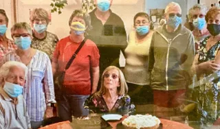 Des personnes debout entourent une personne agée assise devant un gâteau d'anniversaire