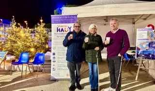 Trois personnes boivent un vin chaud devant un stand de l'AVH