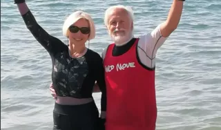 Deux personnes avec les pieds dans l'eau et la mer en arrière plan