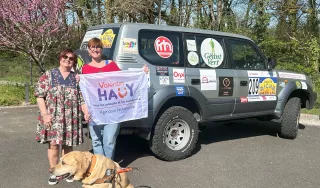 Devant le 4x4 Iris, Laure, Geneviève la Présidente du comité et son chien guide Neigel présentant la banderole du comité