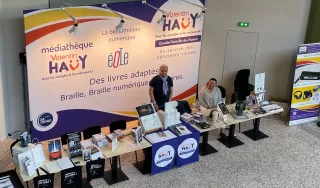 Vue de haut notre stand au festival avec à l'arriére une grande banderole avec les logos du comité et de la médiathèque de l'AVH.