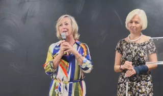 Deux dames debout. Celle de gauche tient un micro.