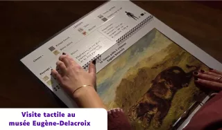 Gros plan sur une personne utilisant un livret de médiation tactile au musée Eugène-Delacroix. Ses mains parcourent des schémas en braille et une reproduction en relief du tableau « La Lionne prête à s'élancer ». Un bandeau indique : « Visite tactile au musée Eugène-Delacroix ».