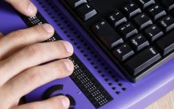 Des mains sur une plage braille en dessous d'un clavier informatique