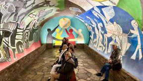 Un groupe de personnes assises dans la chapelle où est exposée l'œuvre "Guerre et Paix" de Picasso
