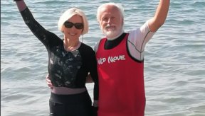 Deux personnes avec les pieds dans l'eau et la mer en arrière plan