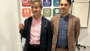 Sylvain Nivard, président de l'association Valentin Haüy (à gauche), et le directeur de la fédération (à droite) posent côte à côte devant un kakémono d'information. Sylvain Nivard, souriant, porte une veste bleu marine sur une chemise à rayures roses et tient une canne blanche. Le directeur porte un costume marron clair sur une chemise bleue. Le panneau derrière eux présente le logo de l'association « Valentin Haüy : Agir pour l'autonomie » ainsi que des icônes colorées illustrant leurs services : médiathè